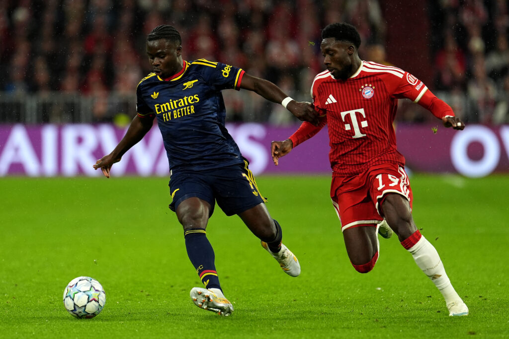 Bukayo Saka of Arsenal runs with the ball under pressure from Alphonso Davies of Bayern Munich during the Champions League clash at the Allianz Arena